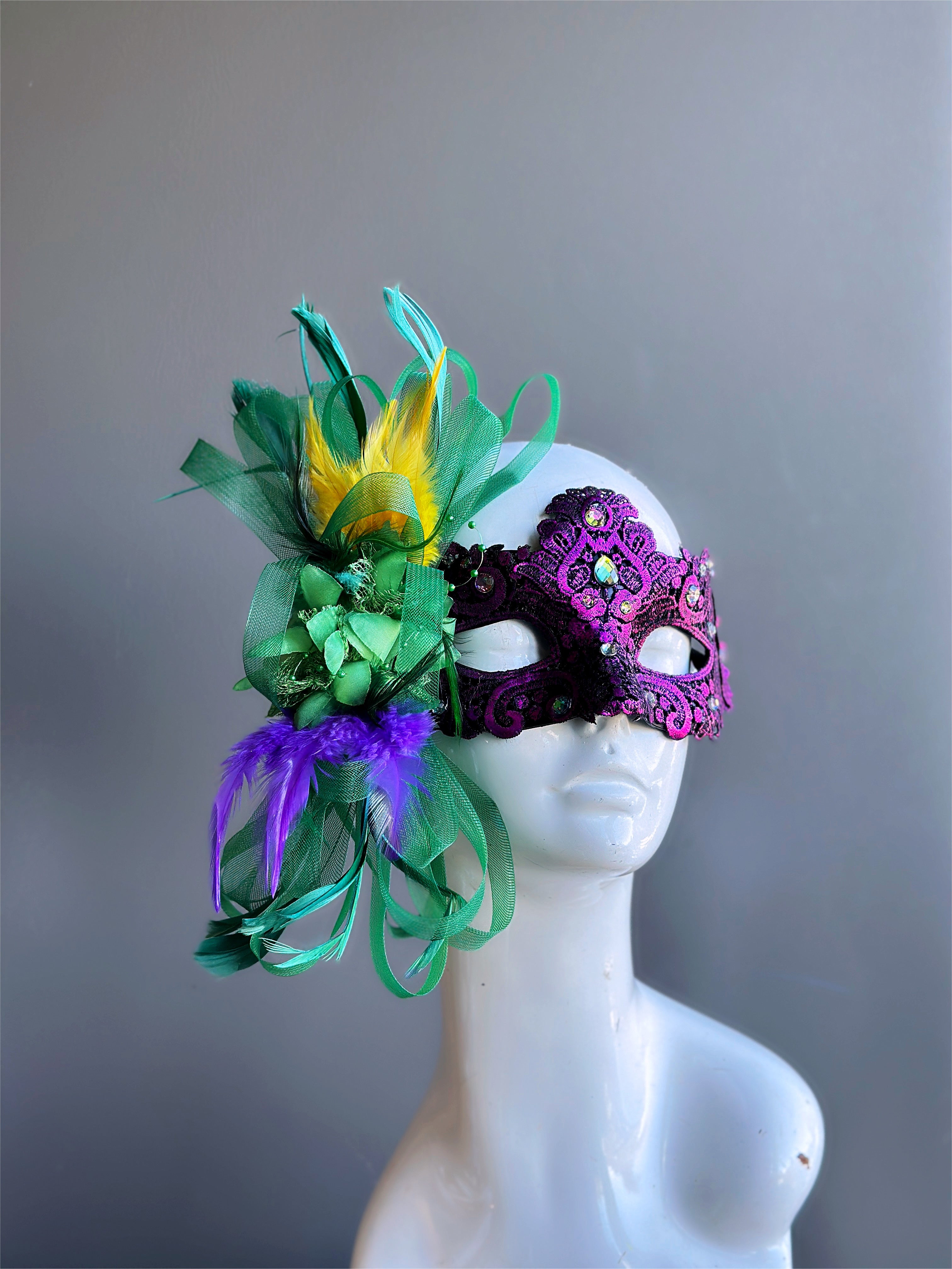 Purple Mardi Gras masquerade mask for women with green floral ribbons and yellow, purple, and green feathers.
