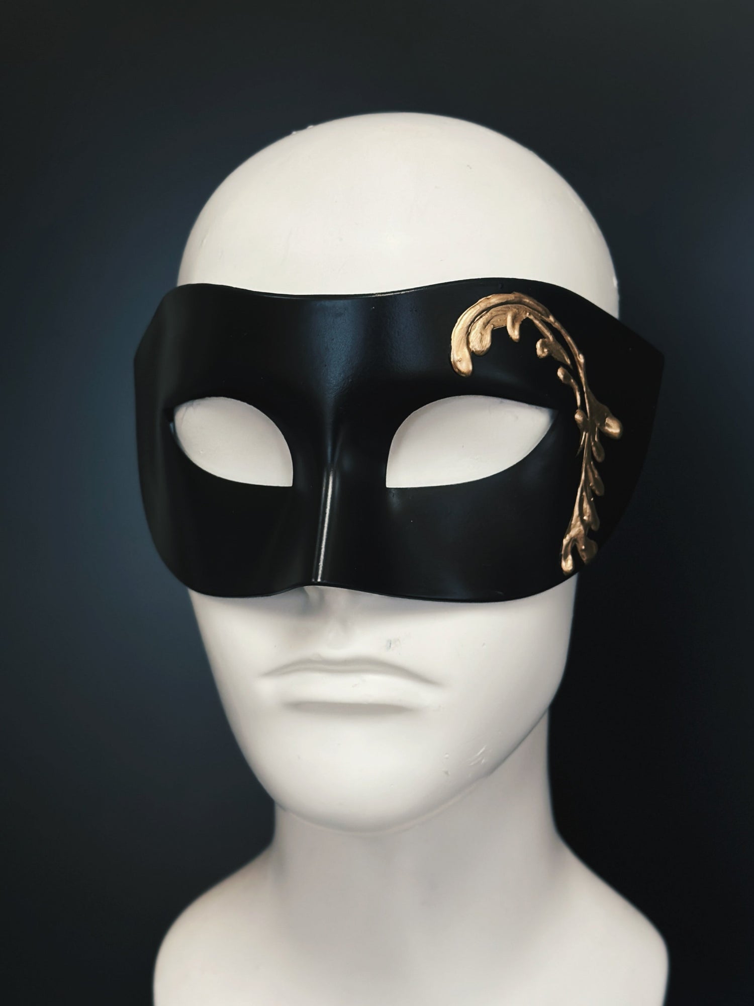 Black masquerade mask base with a gold hand-painted design on the side.