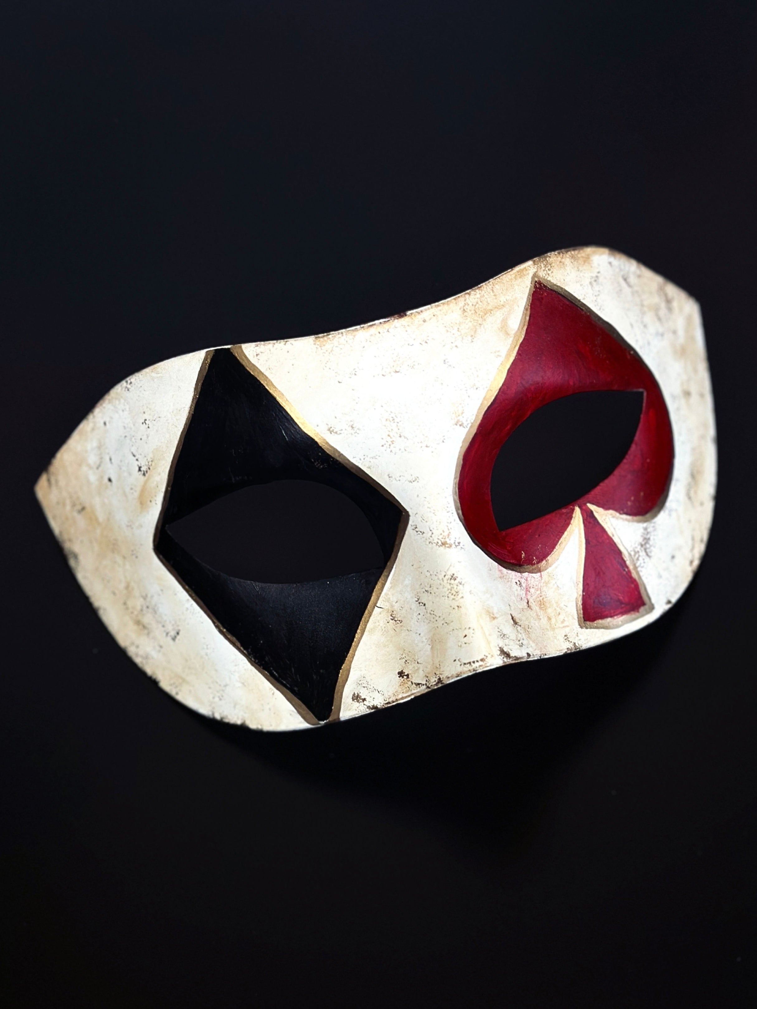 Diamond and spade card symbols in black and red over the eyes on a masquerade mask.
