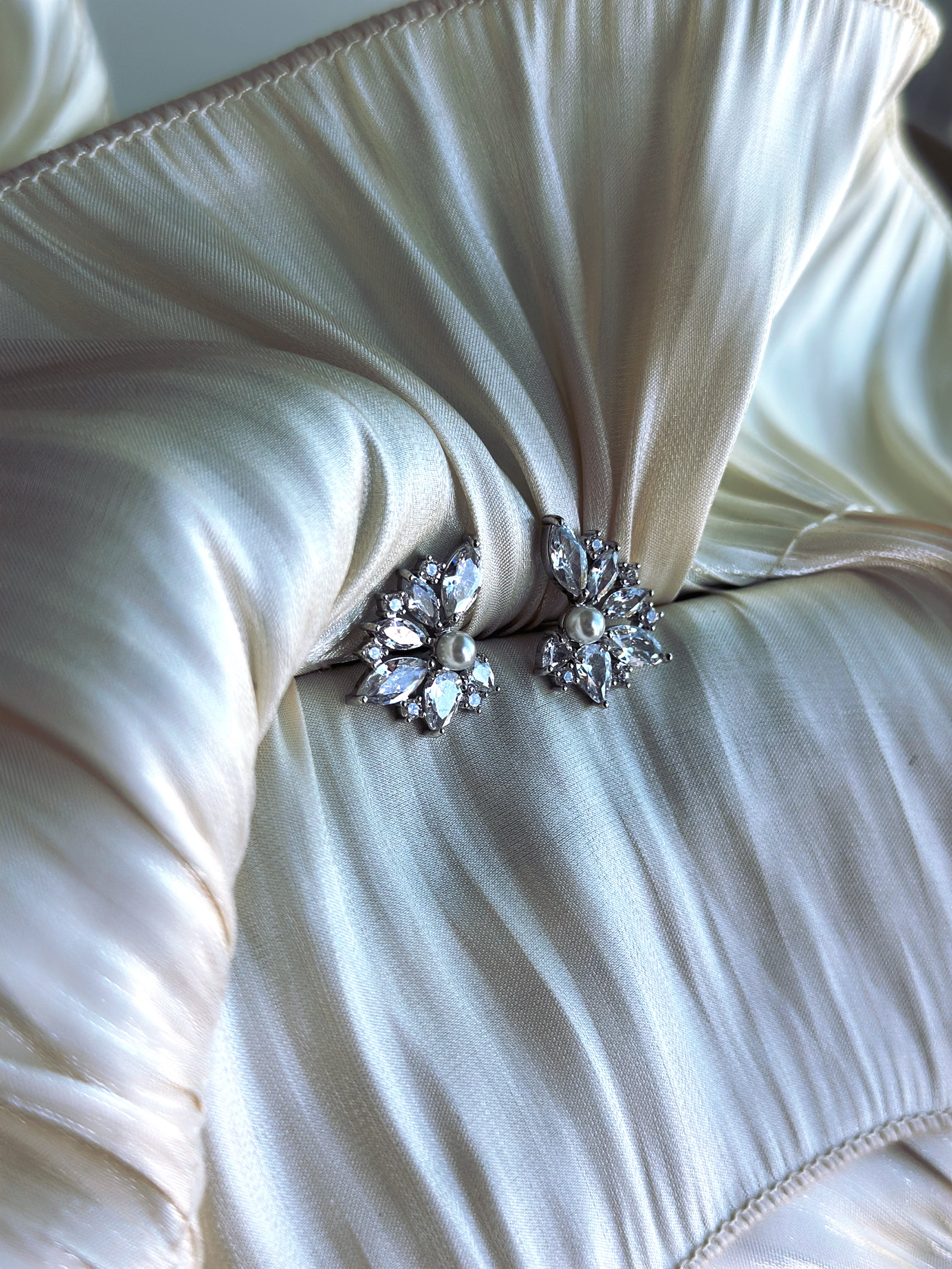 Silver floral crystal stud earrings with pearl center on ivory satin