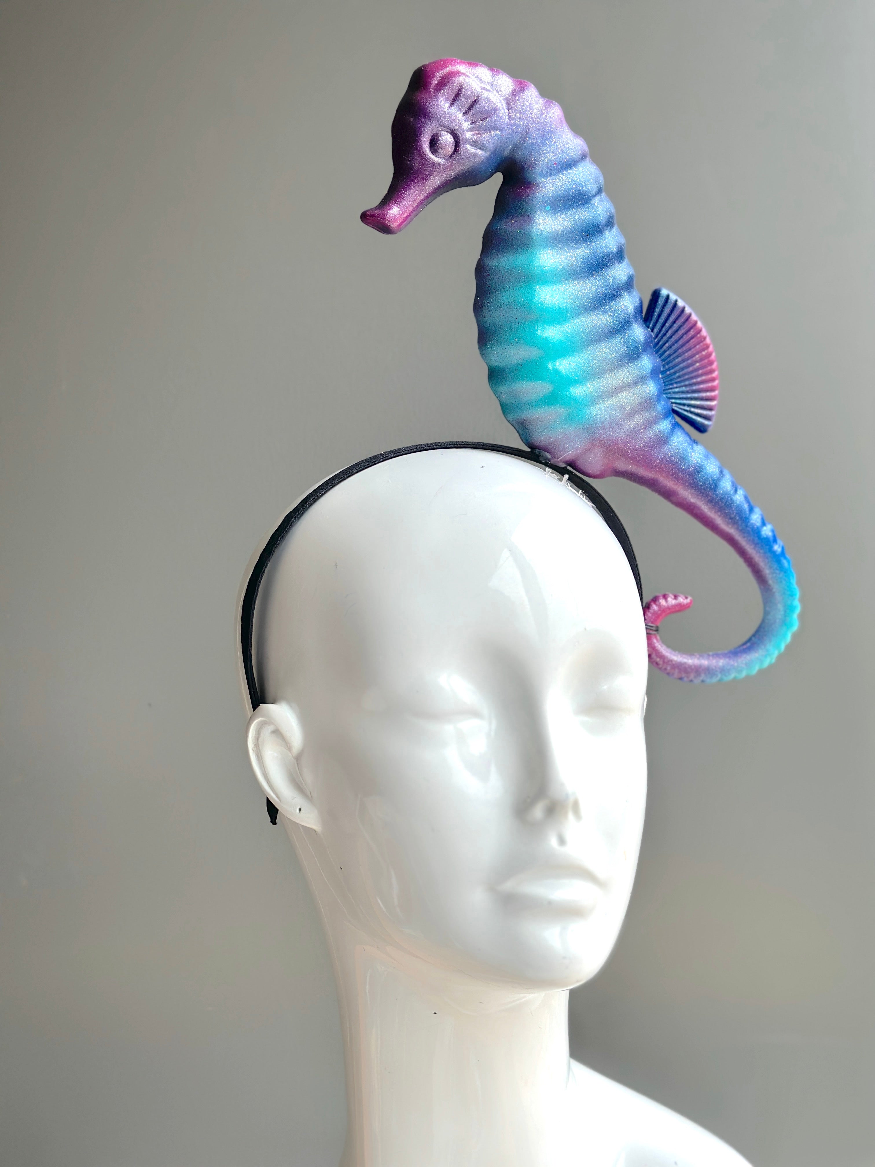 Pastel seahorse fascinator in iridescent purple, blue, and pink on a sleek headband, ideal for ocean-themed events and unique fashion.