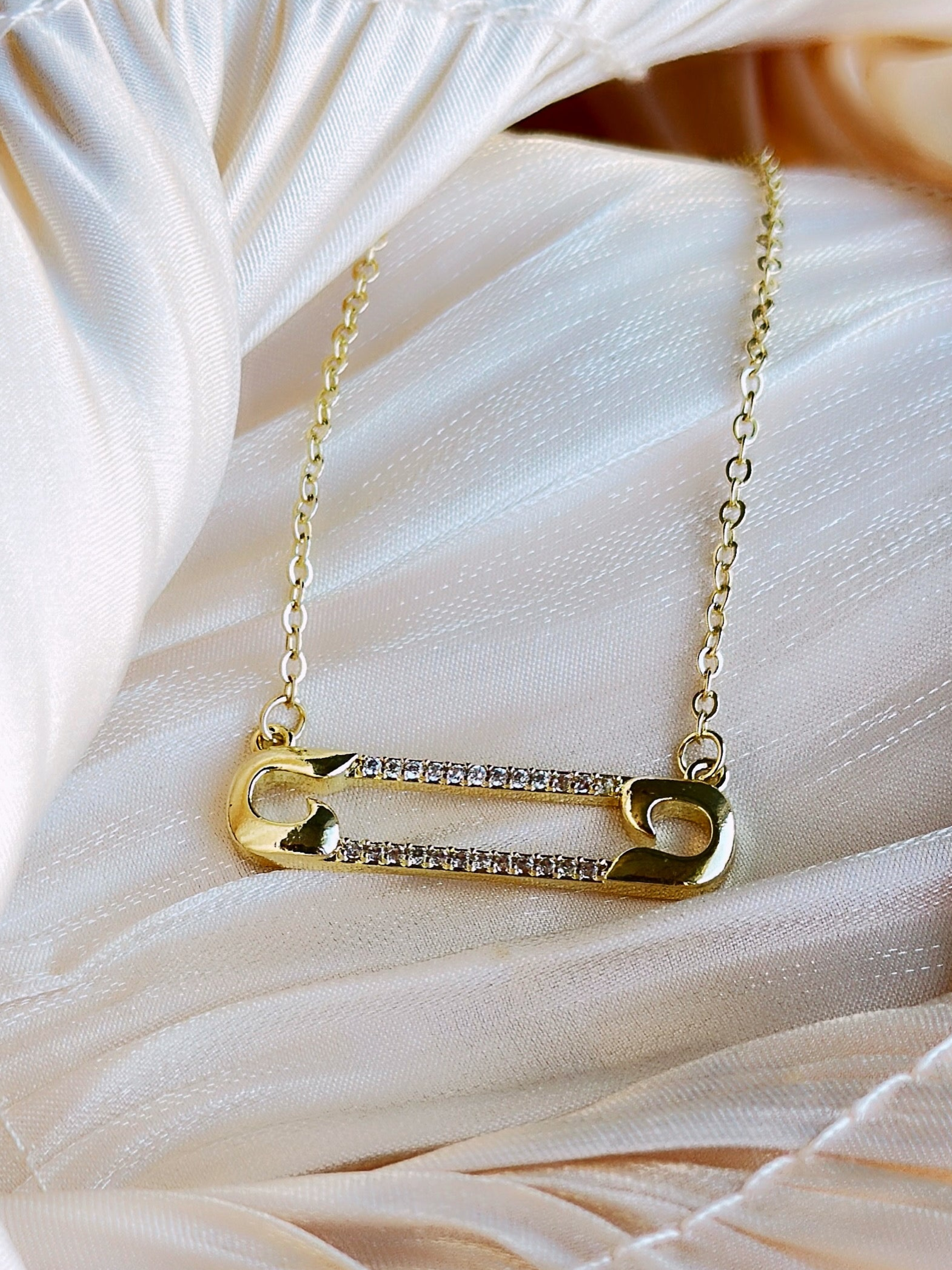 Gold plated necklace with a gold safety pin pendant adorned with clear crystals.