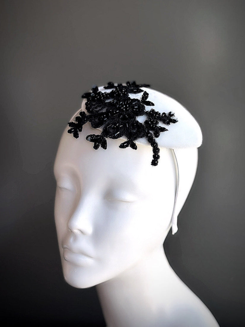 White fascinator hat with dramatic black lace applique, elegant for formal events and statement fashion moments.
