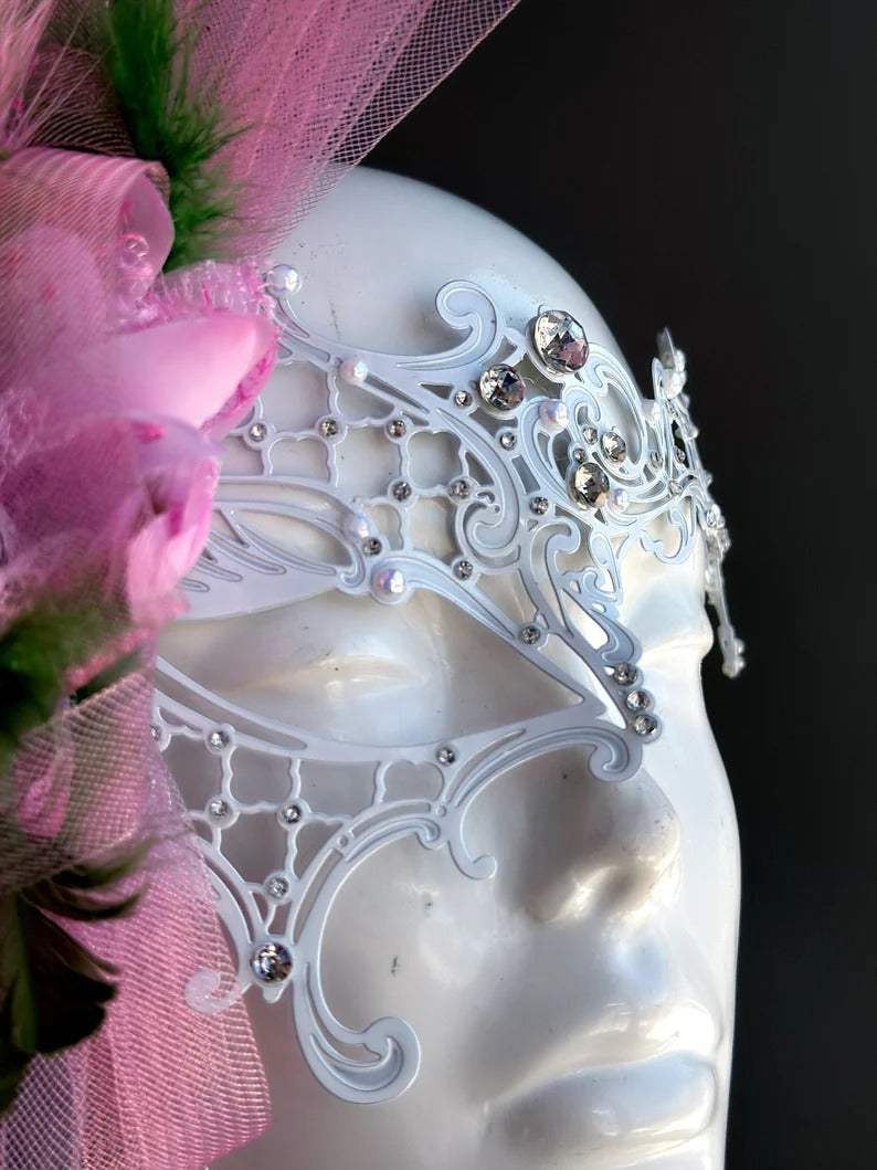 Elegant white lace masquerade mask with pink feathers and rhinestones for women’s prom, carnival, and party looks.