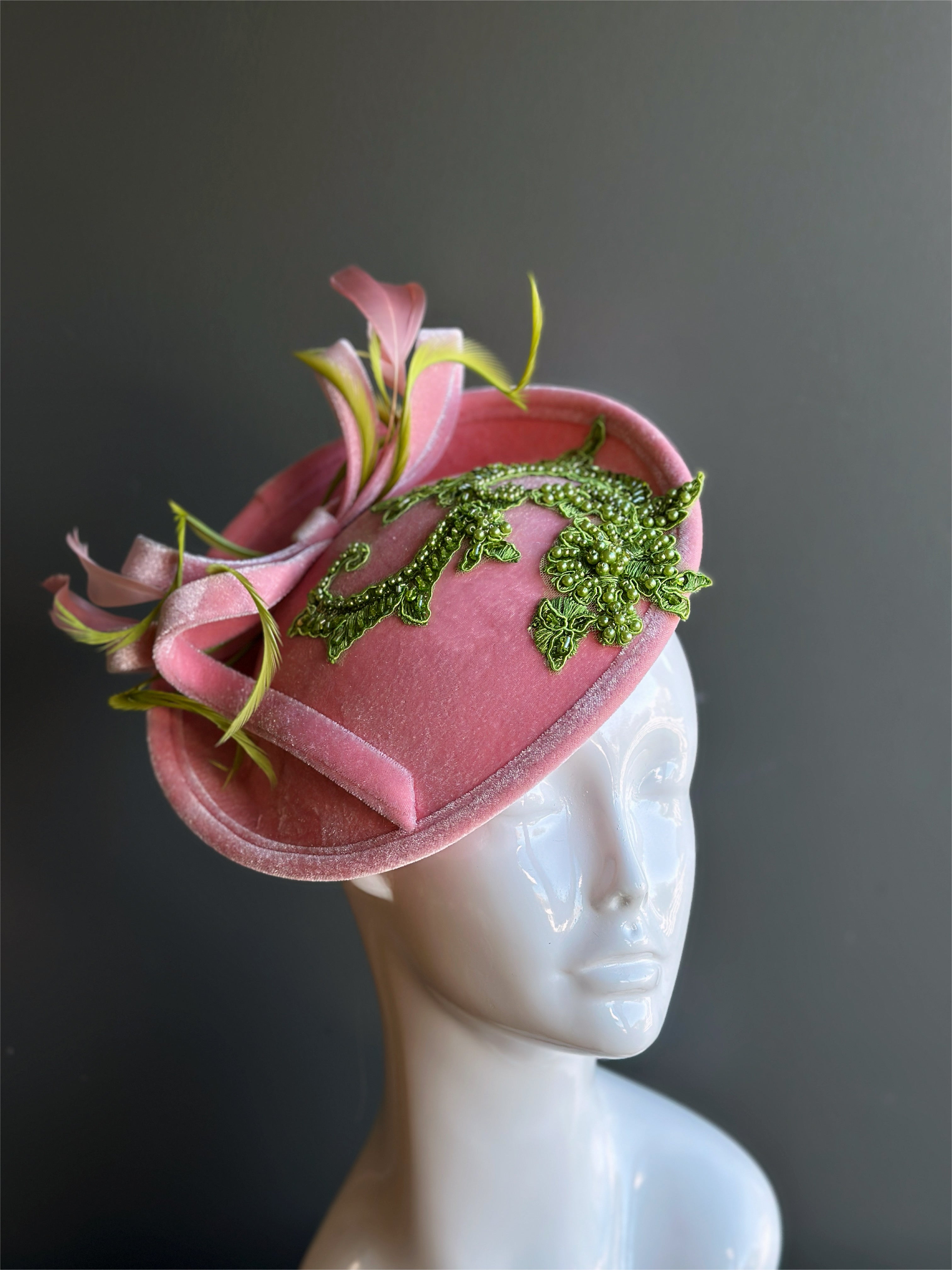 Pink velvet fascinator hat with green floral applique and feathers.