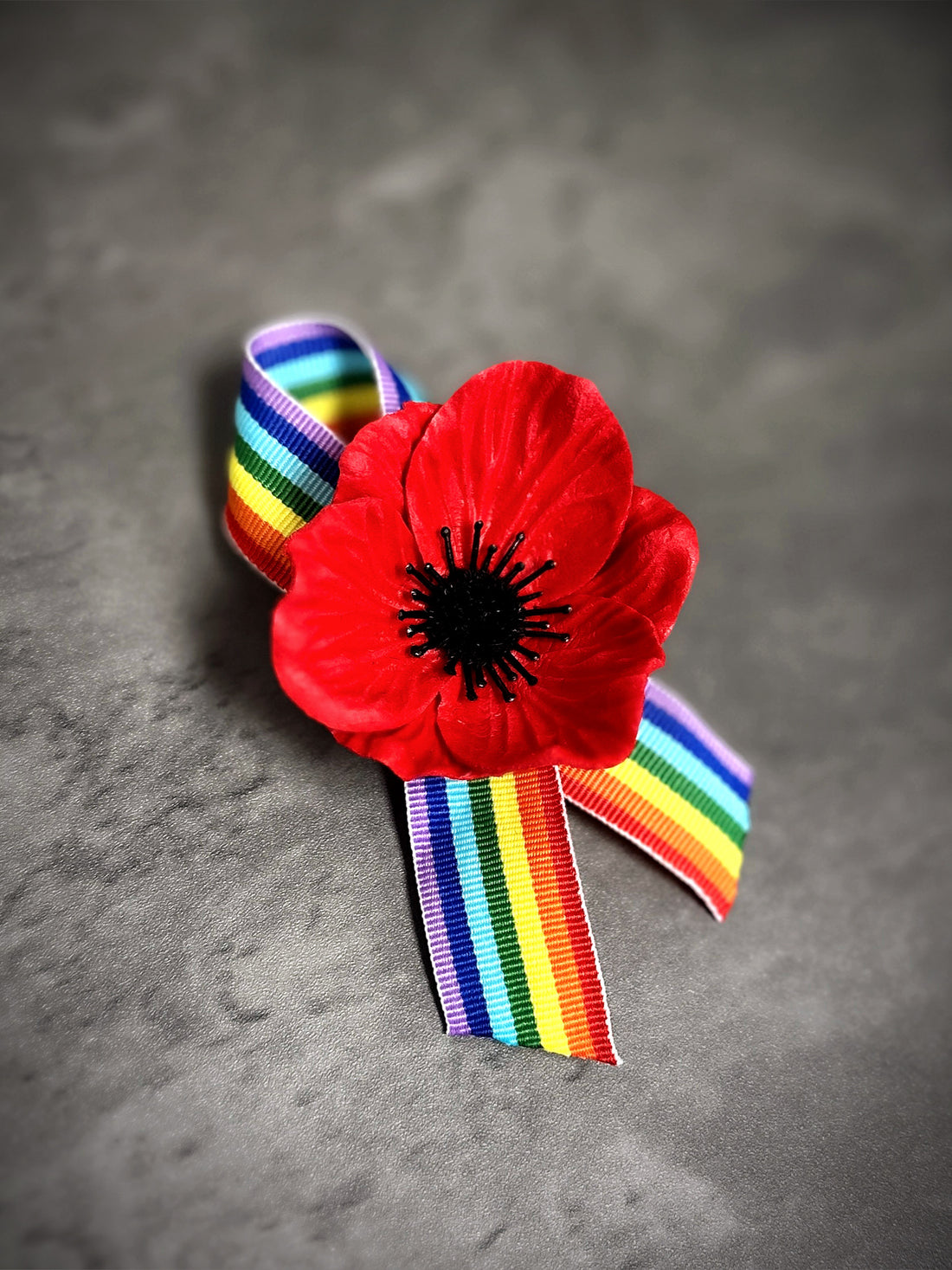 Rainbow pride ribbon pin with red poppy flower accent for LGBTQ+ events and remembrance