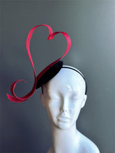 Red heart fascinator hat with sculpted ribbon design.