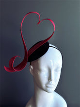 Red heart fascinator hat with sculpted ribbon design.