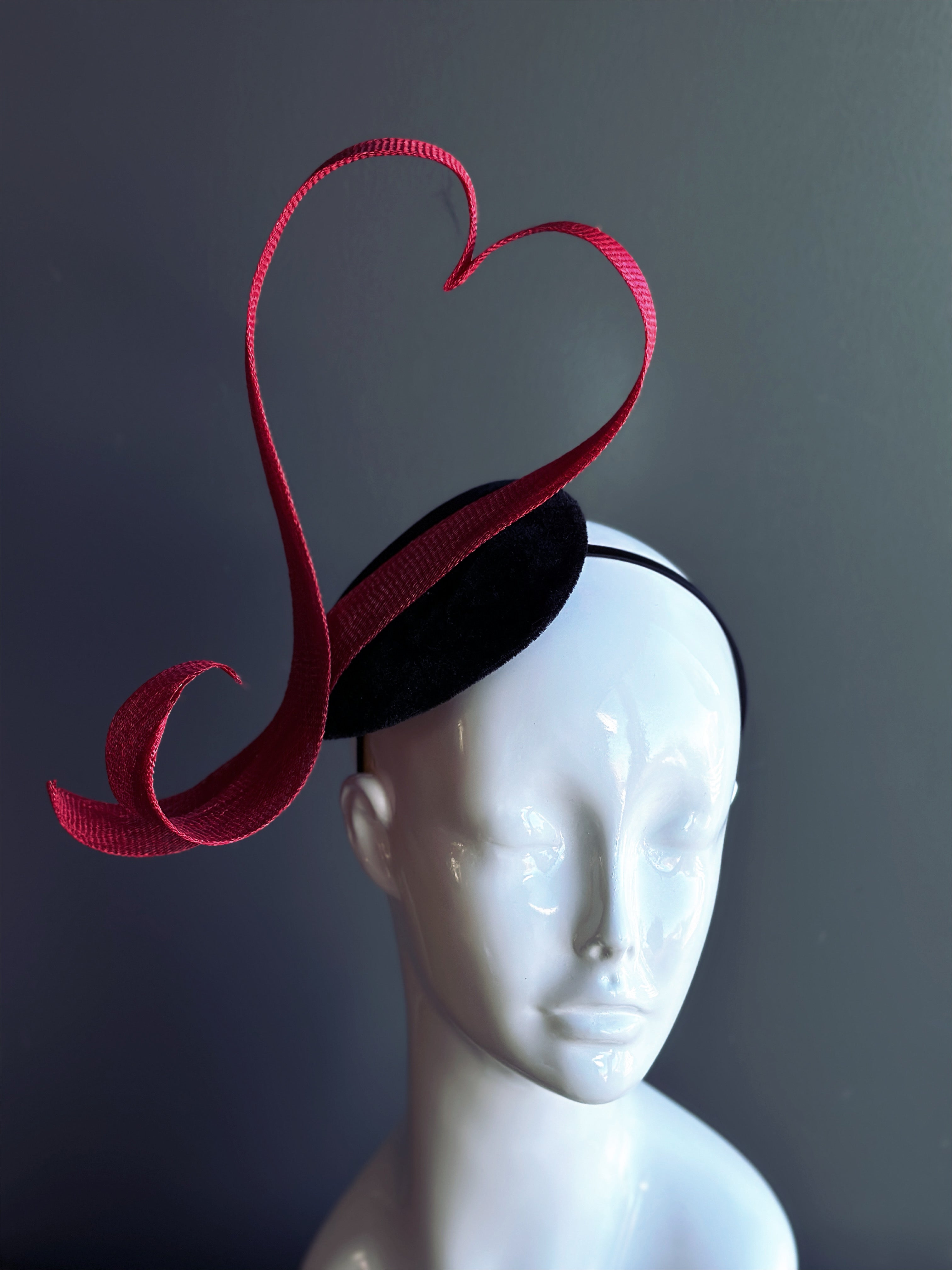 Red heart fascinator hat with sculpted ribbon design.