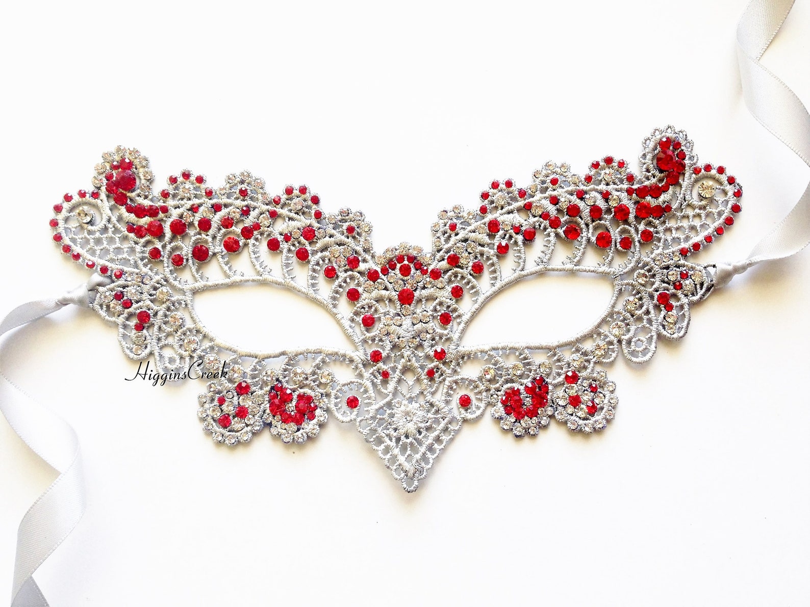 Silver lace masquerade mask adorned with red rhinestones and ribbon ties