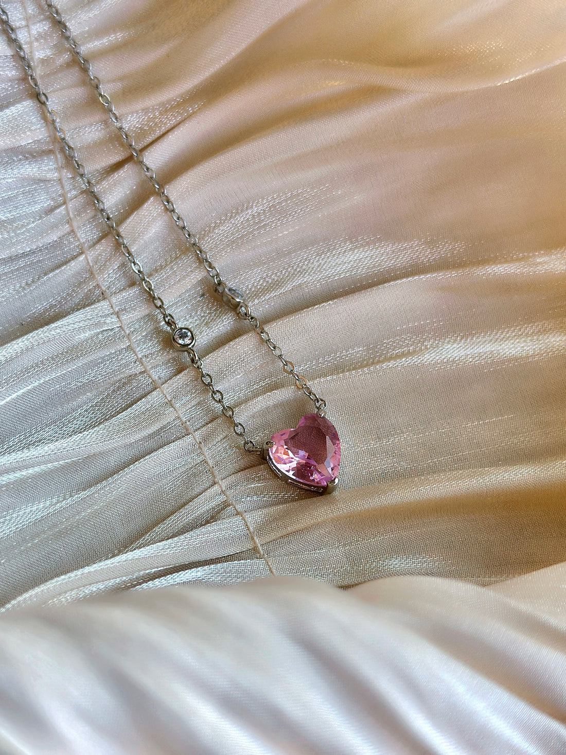 Silver chain necklace with pink heart-shaped crystal pendant .