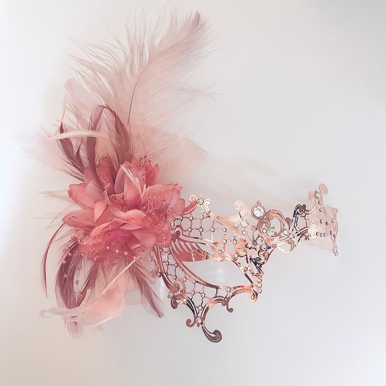 Elegant rose gold filigree masquerade mask with blush feathers and floral detail, ideal for weddings, proms, and masquerade balls.