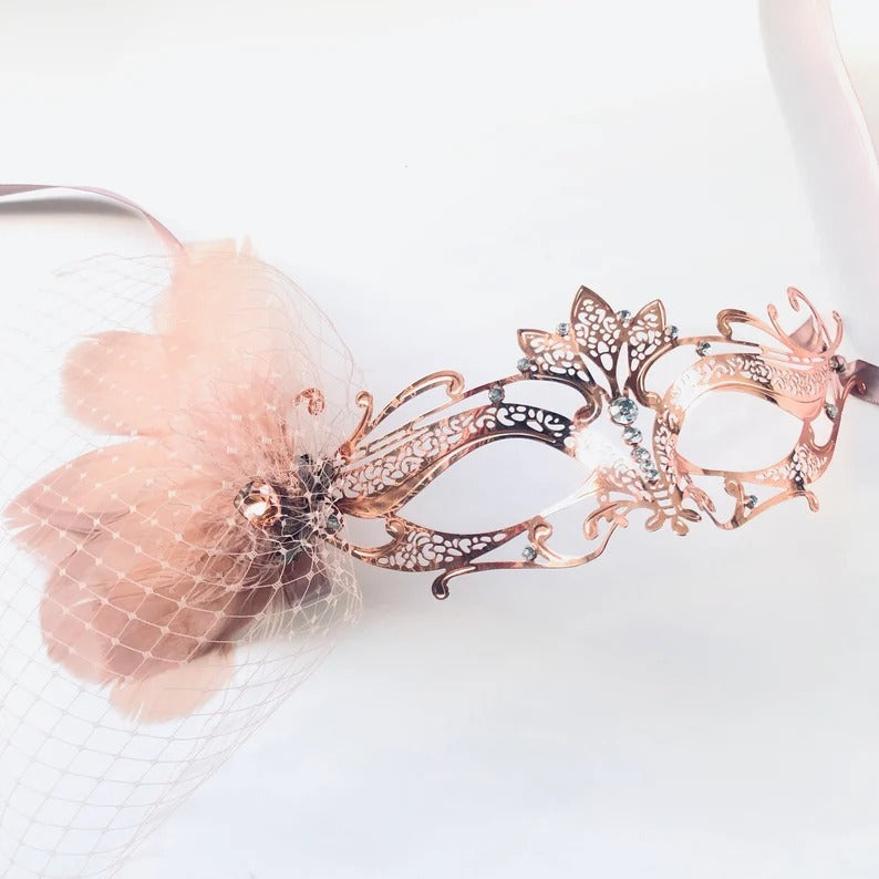 Elegant rose gold masquerade mask with filigree design, flower, netting, and rhinestones for weddings, Venetian balls, and prom parties.