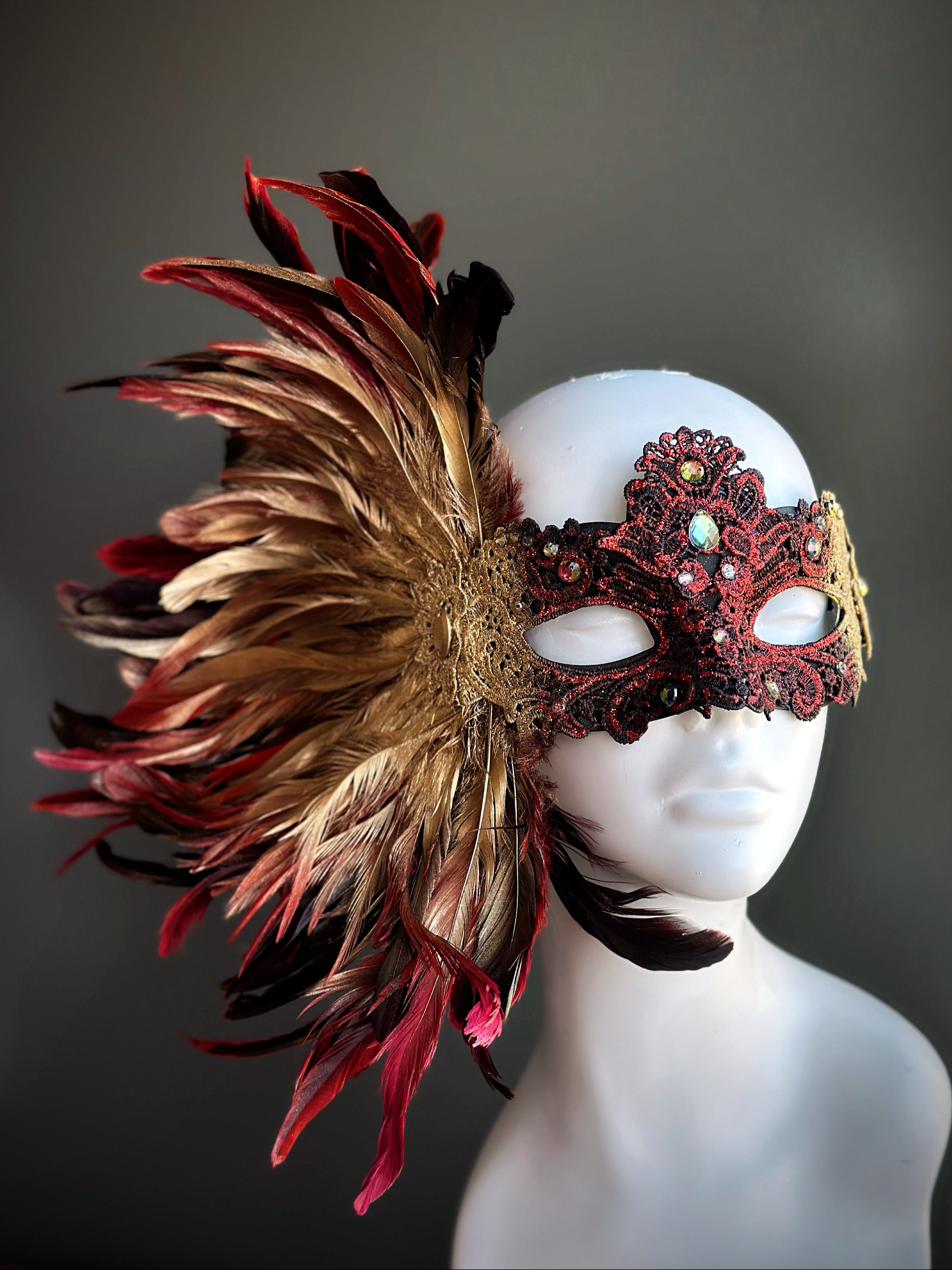 Red and gold feather masquerade mask with opulent plume design and ornate lace accents.