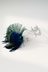 Silver filigree mask with blue and green feathers and jewel accent, designed for masquerade parties, weddings, and proms.