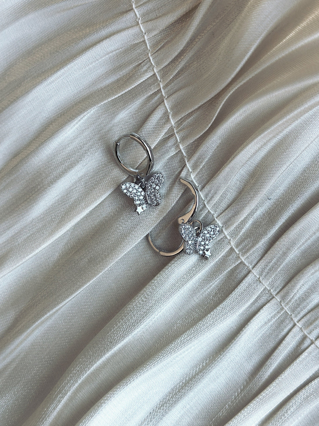 Silver butterfly drop earrings with crystals on soft champagne satin fabric
