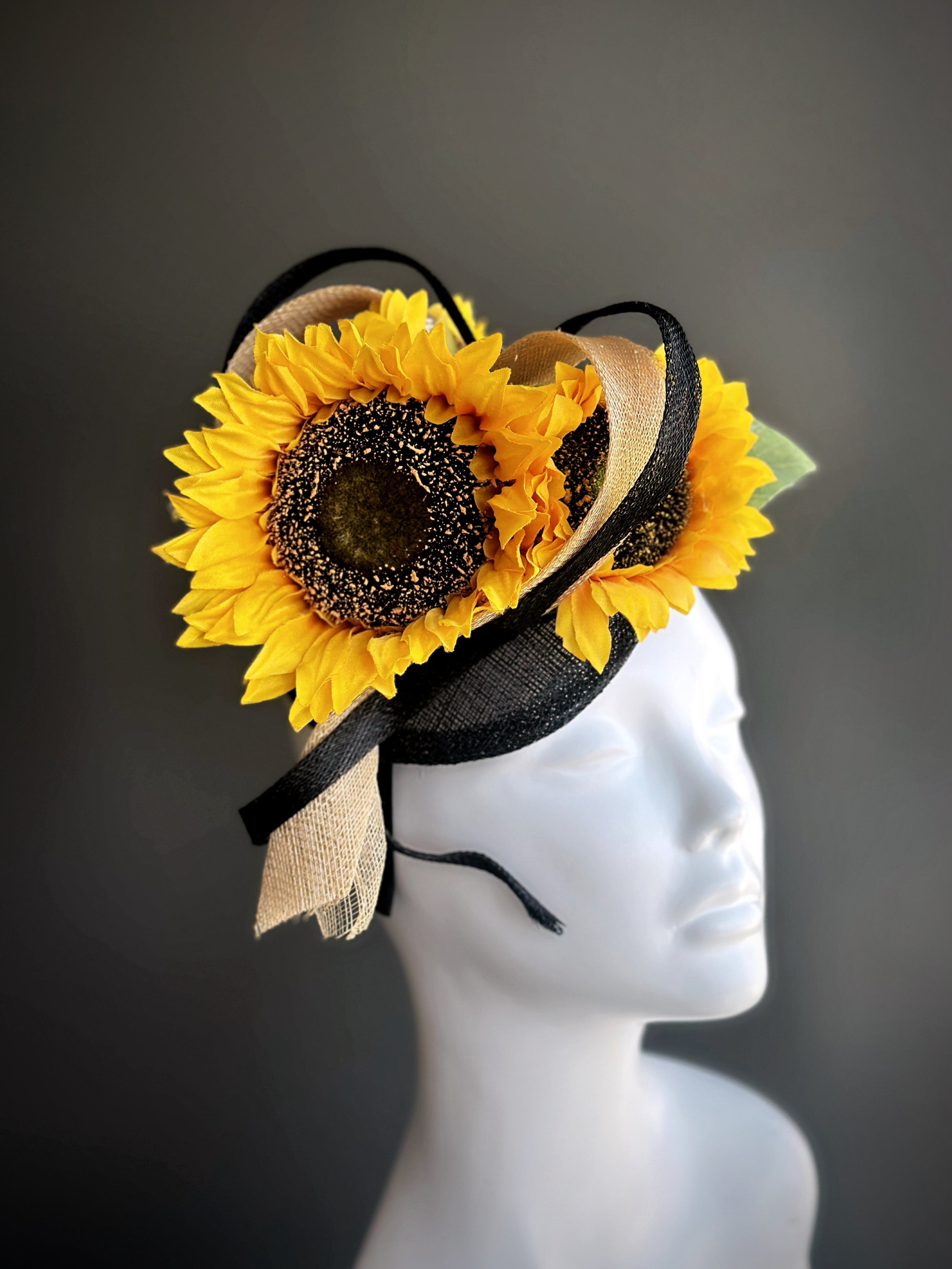 Fascinator hat with large yellow sunflowers wrapped in black and gold sinamay heart loops