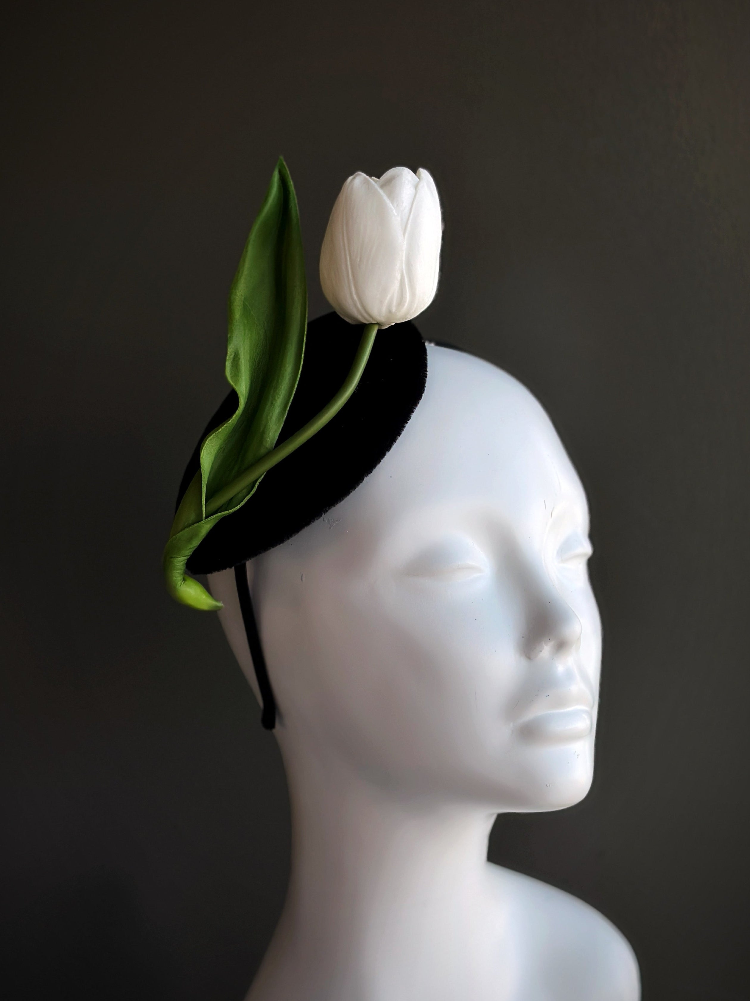 White tulip fascinator with green leaves on a black base.