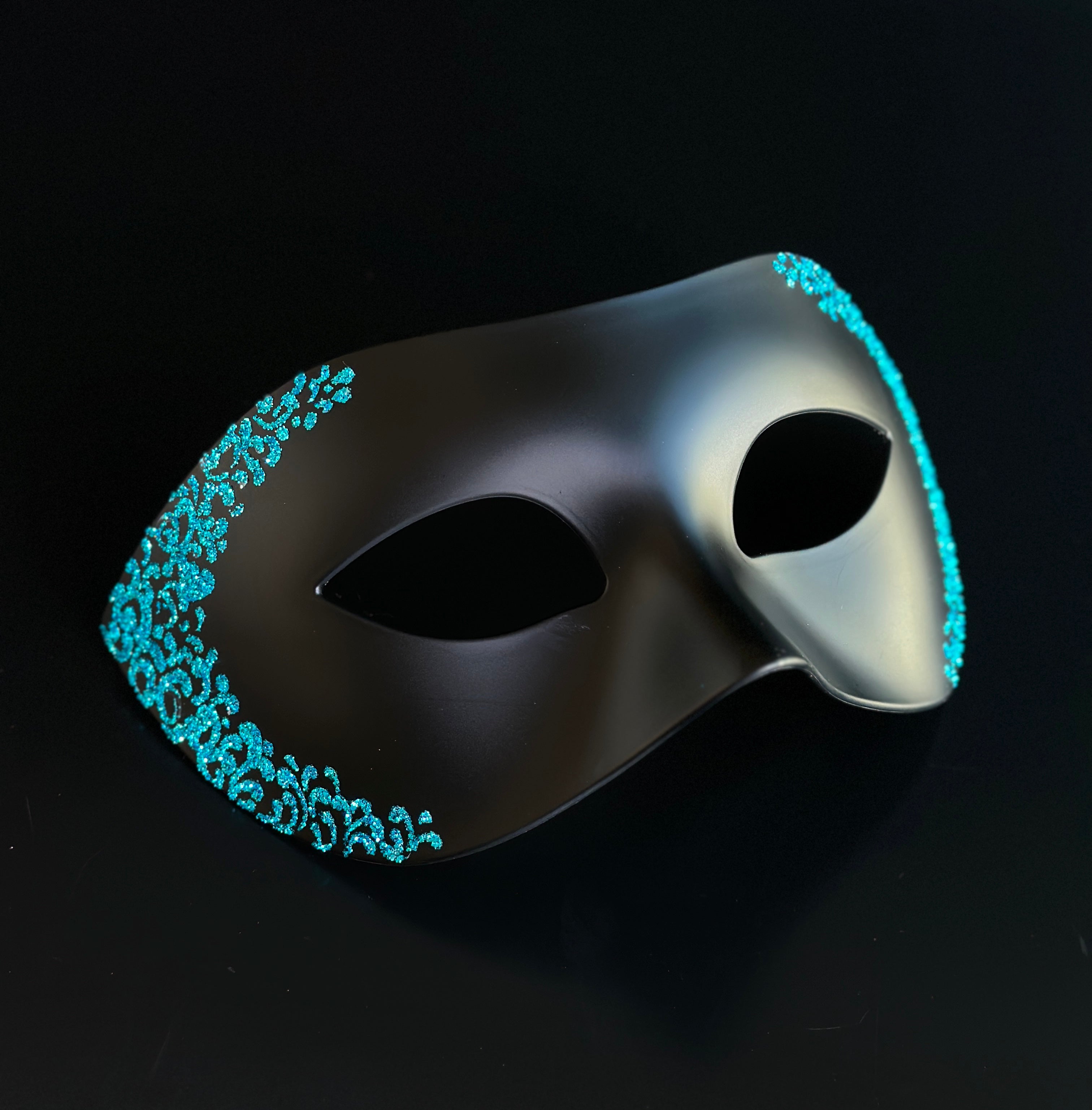 Matte black Venetian Phantom masquerade mask with turquoise glitter filigree trim, lightweight half-face costume mask for masquerade balls, Mardi Gras, Halloween, Venetian carnival, cosplay, weddings, black-tie events, theatrical performances, and formal parties.