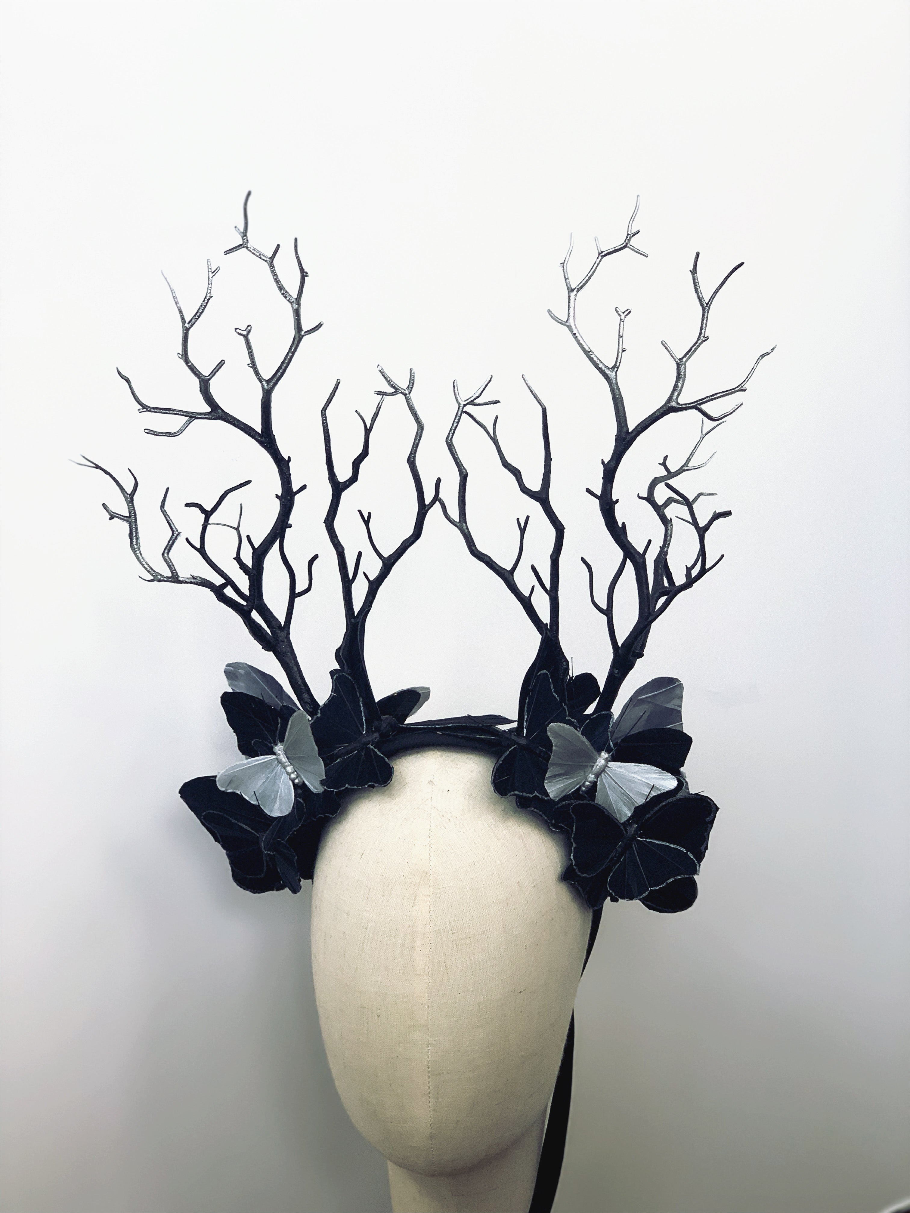 Black antler headdress with silver butterflies and intricate branch-like details.