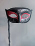 Black handheld masquerade mask with red glitter accents and ornate swirl details