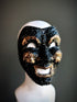 Venetian comedy mask in black with gold detailing, featuring an expressive smiling design and intricate raised accents.