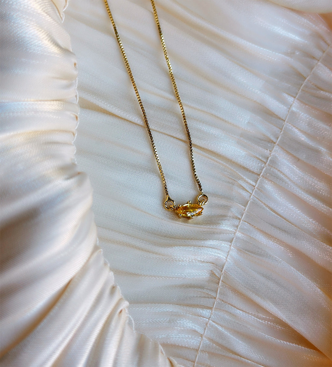 Gold necklace with a single marquise-cut yellow gemstone pendant.
