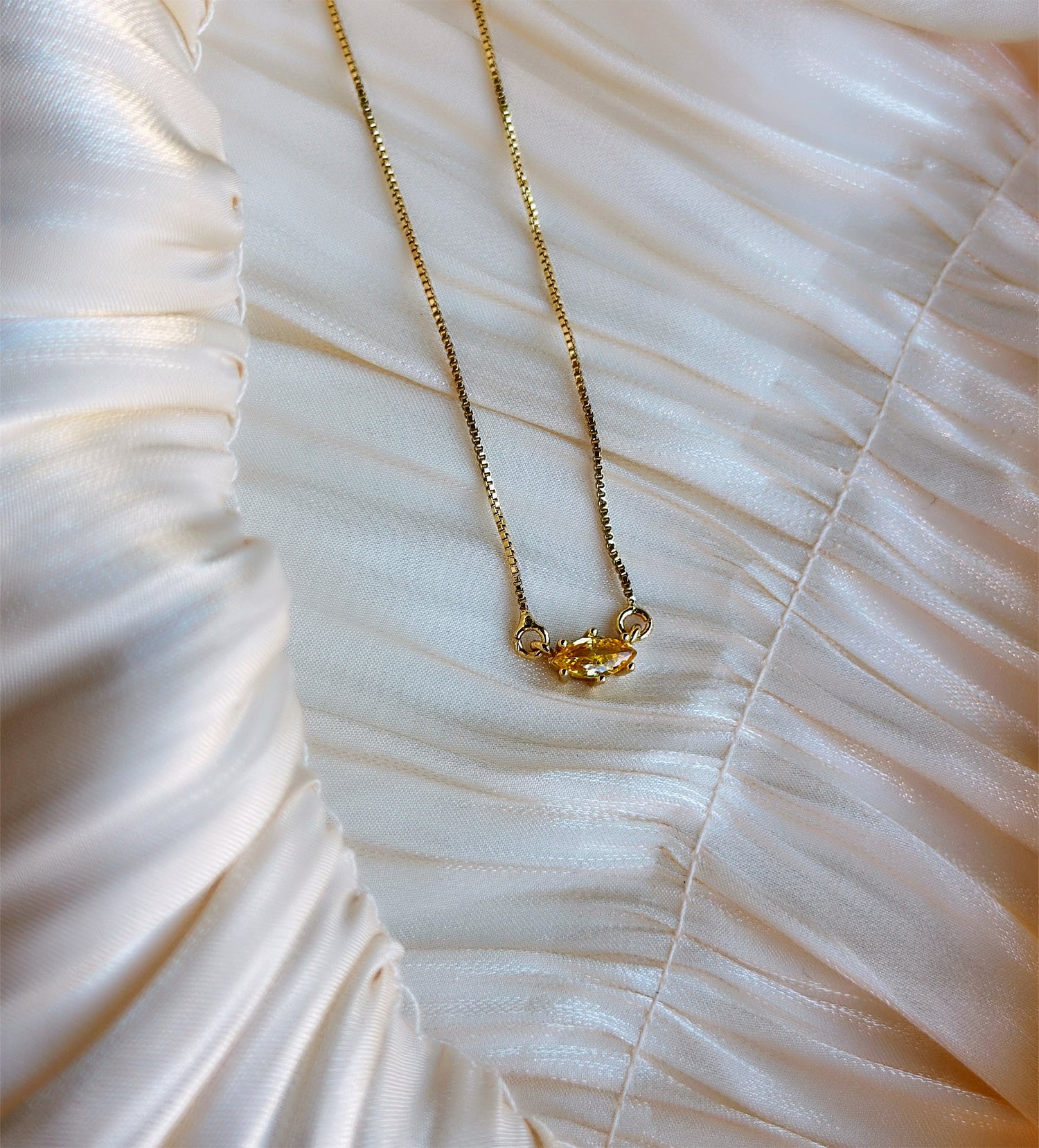 Gold necklace with a single marquise-cut yellow gemstone pendant.