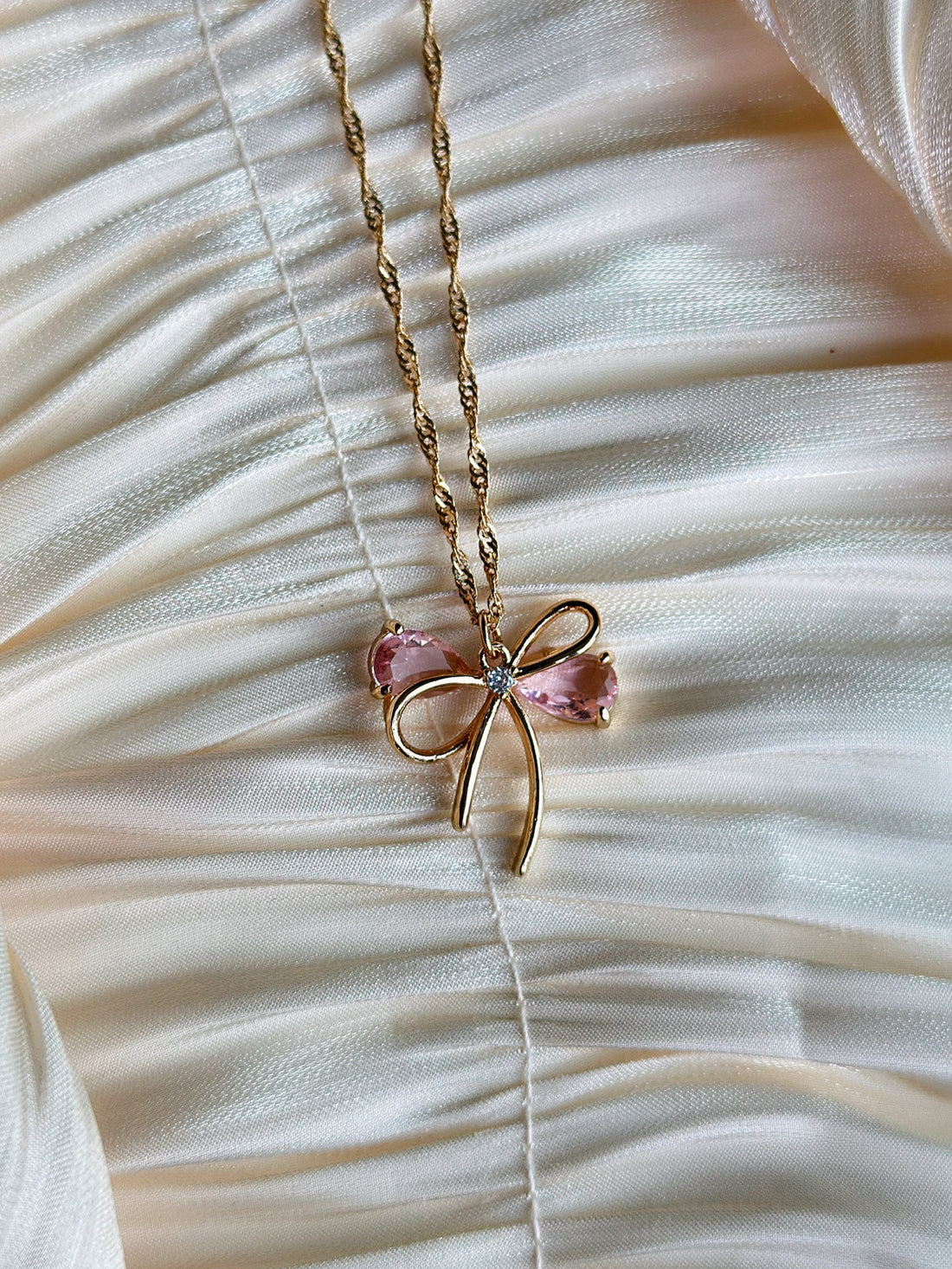 Gold bow pendant necklace with pink gemstone accents on a twisted gold chain.
