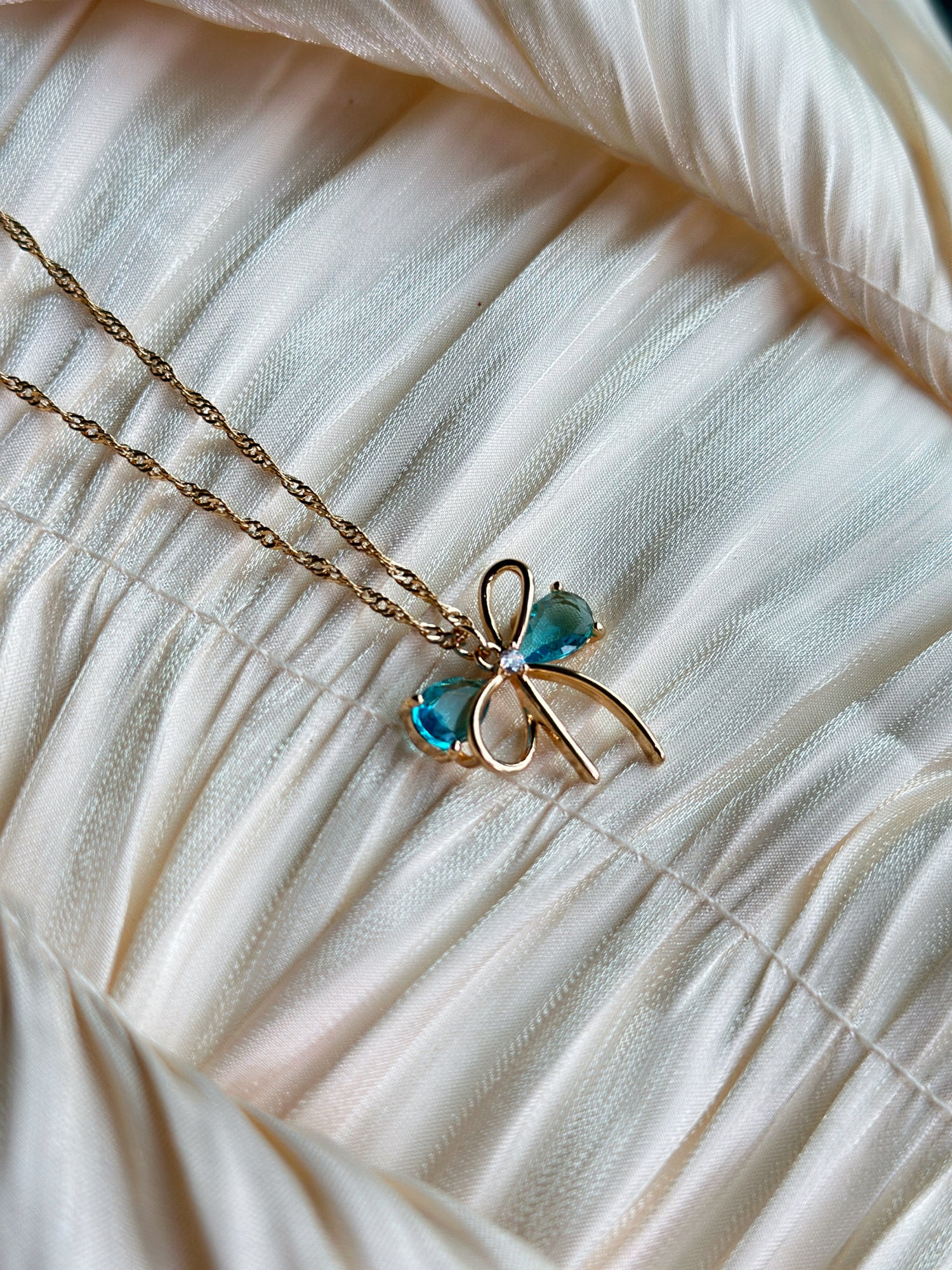 Gold bow pendant necklace with aqua gemstone accents on a twisted gold chain.