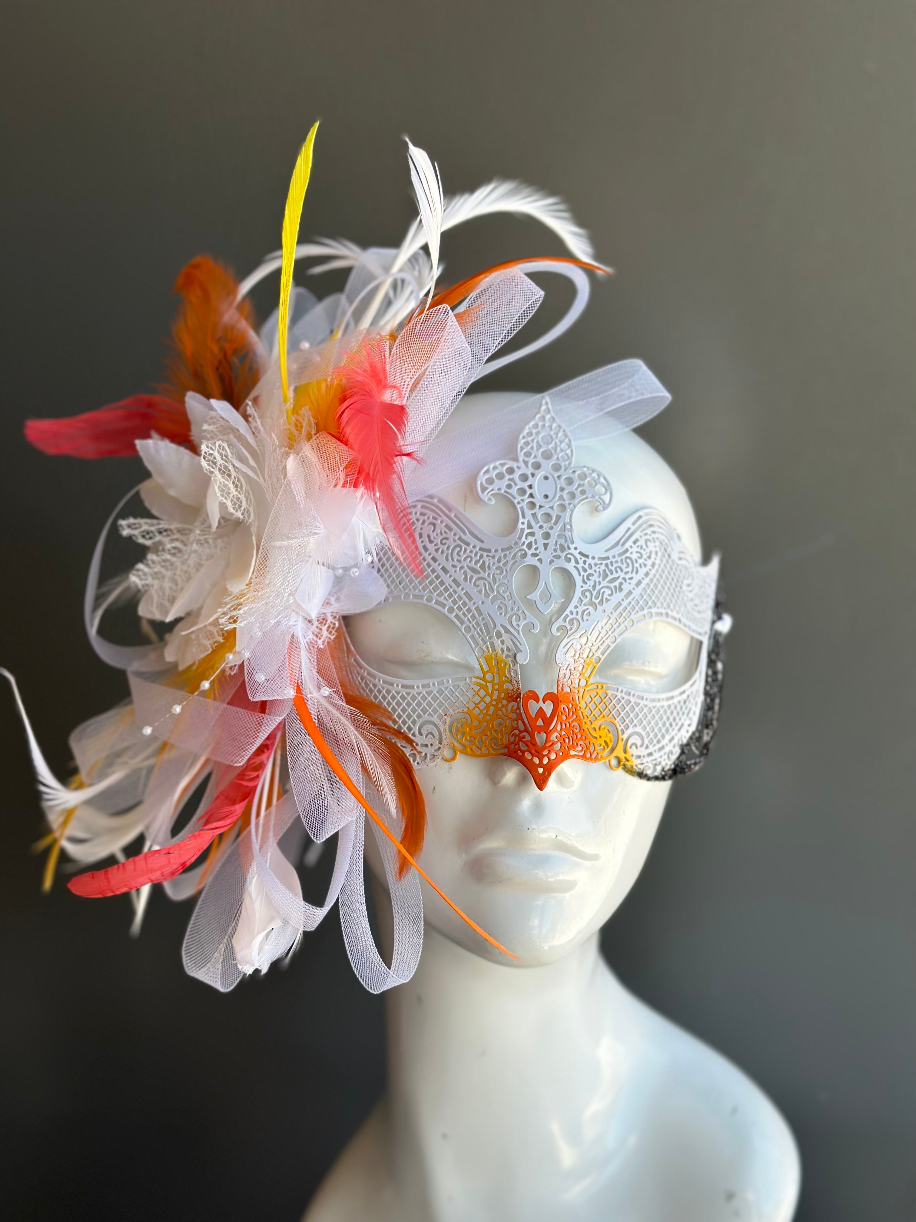 White metal masquerade mask with orange and yellow accents and orange and yellow feathers.
