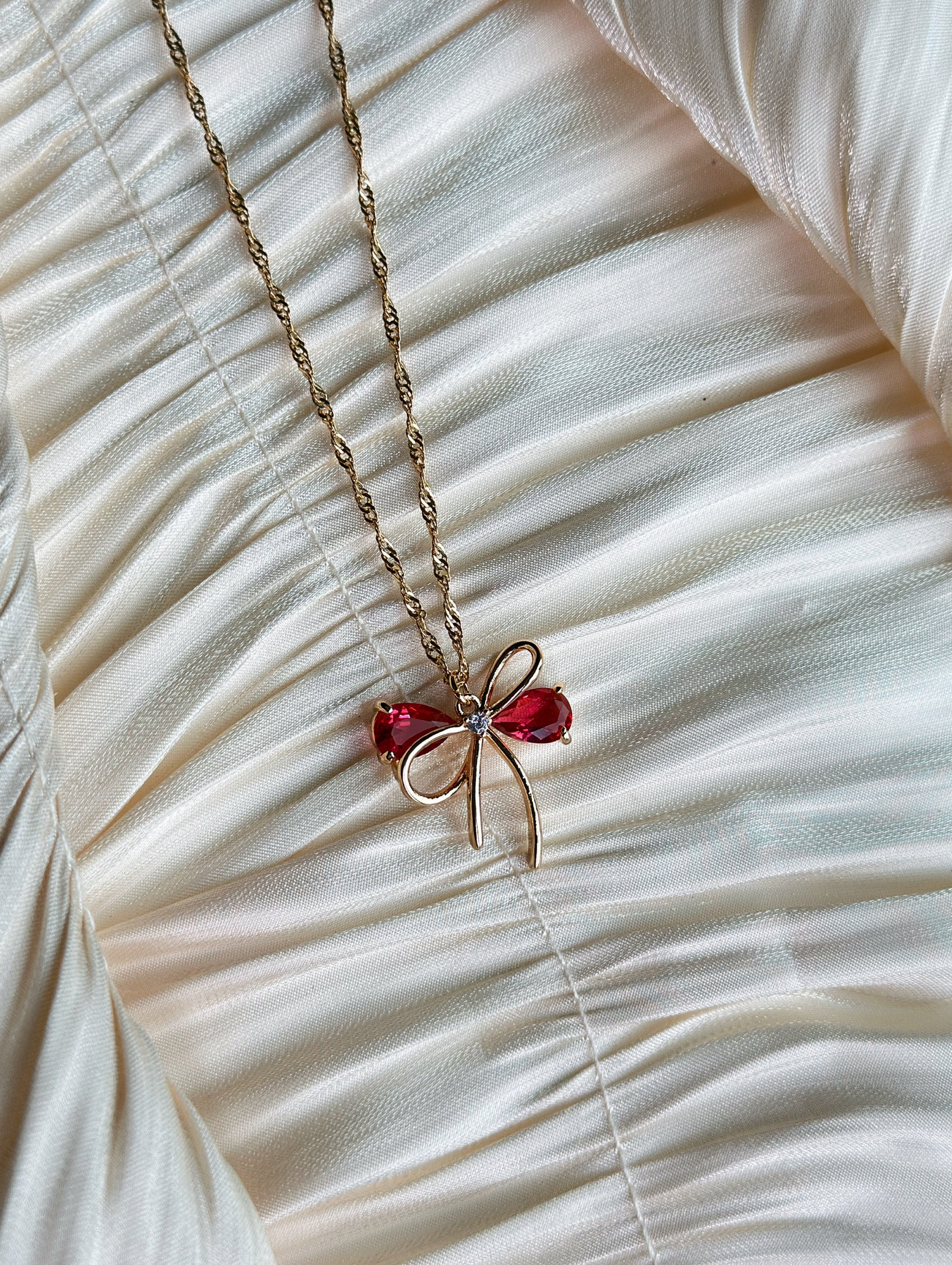 Gold bow pendant necklace with red gemstone accents on a twisted gold chain.
