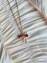 Gold bow pendant necklace with red gemstone accents on a twisted gold chain.