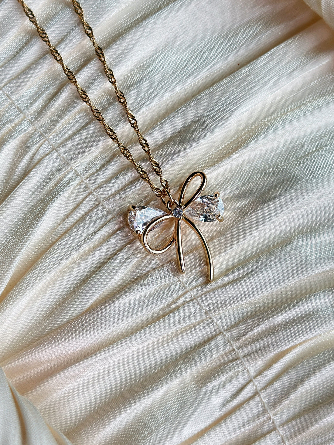 Gold bow pendant necklace with clear gemstone accents on a twisted gold chain.
