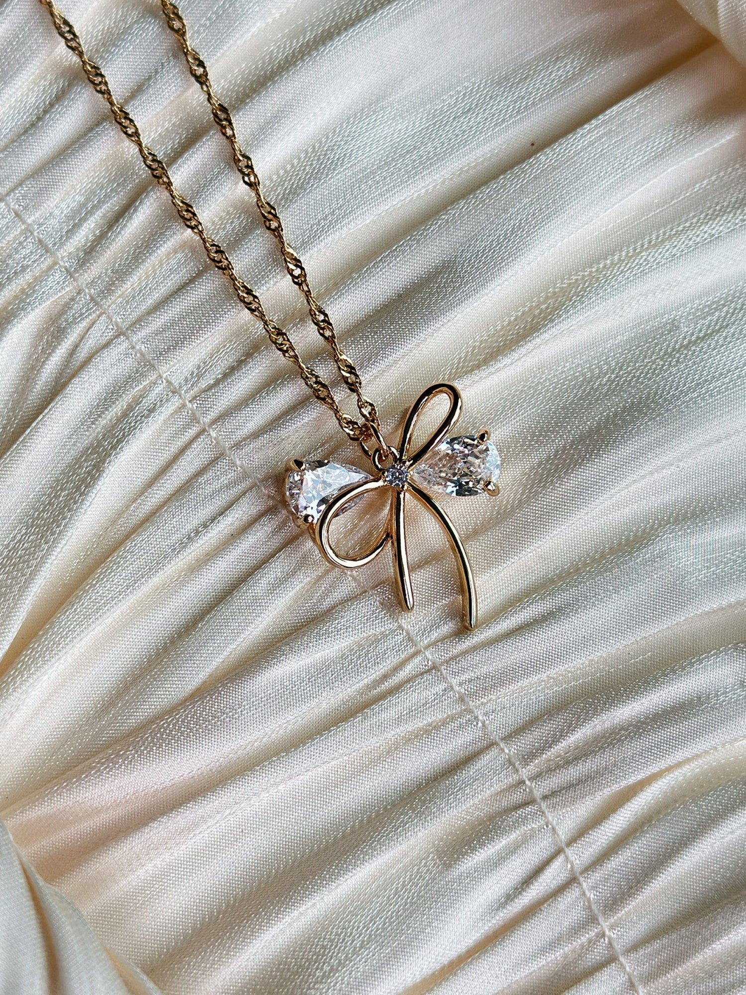 Gold bow pendant necklace with clear gemstone accents on a twisted gold chain.
