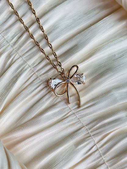 Gold bow pendant necklace with clear gemstone accents on a twisted gold chain.
