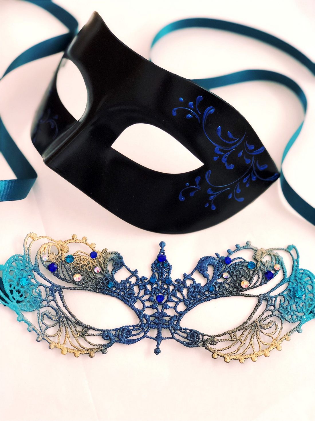 Couple’s masquerade mask set with a teal and gold lace rhinestone women’s mask and a sleek black men’s mask with blue scrollwork.