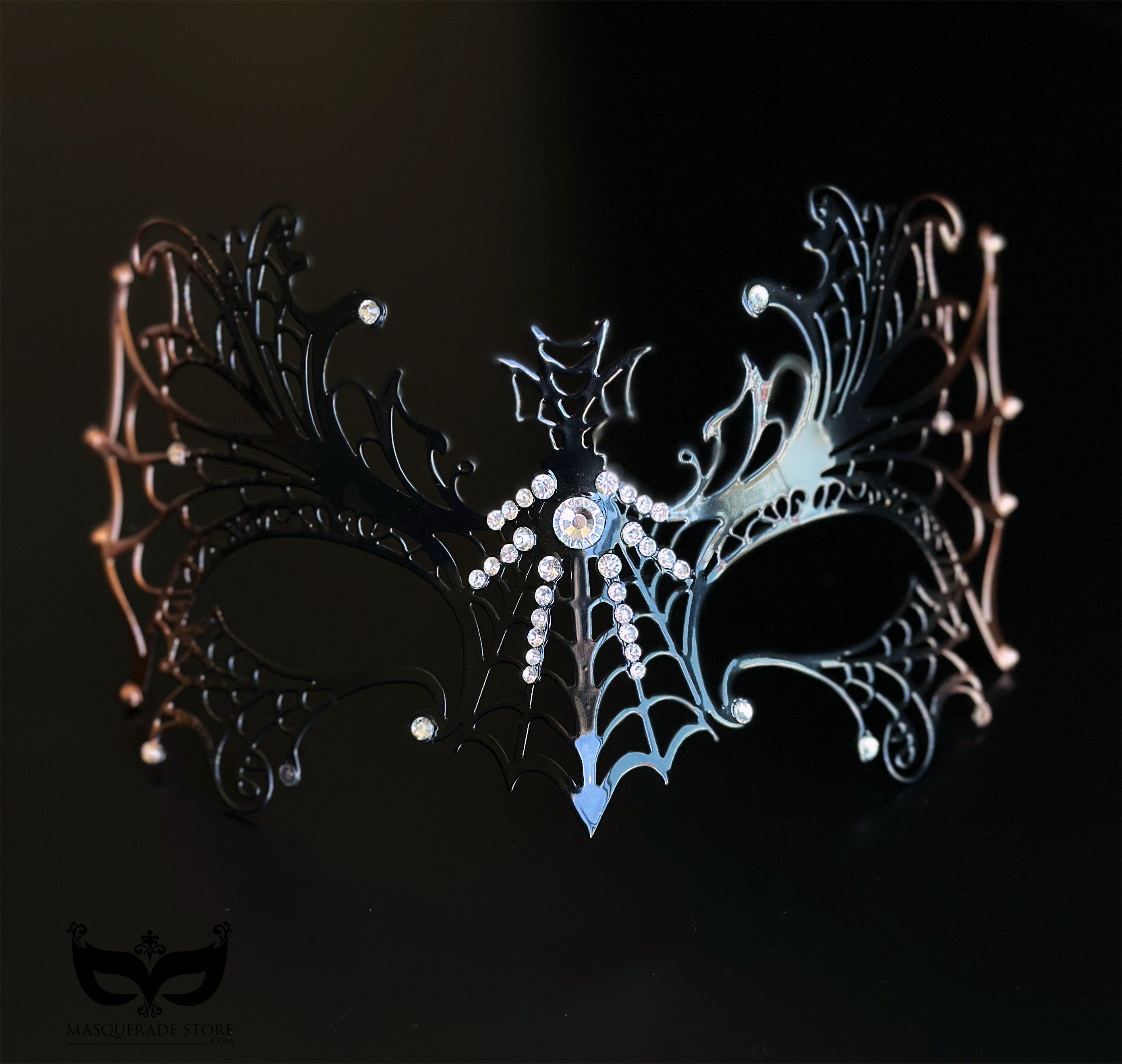 Black and bronze spiderweb masquerade mask with metal filigree openwork, crystal accents, winged gothic details, and Halloween styling.