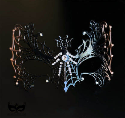 Black and bronze spiderweb masquerade mask with metal filigree openwork, crystal accents, winged gothic details, and Halloween styling.