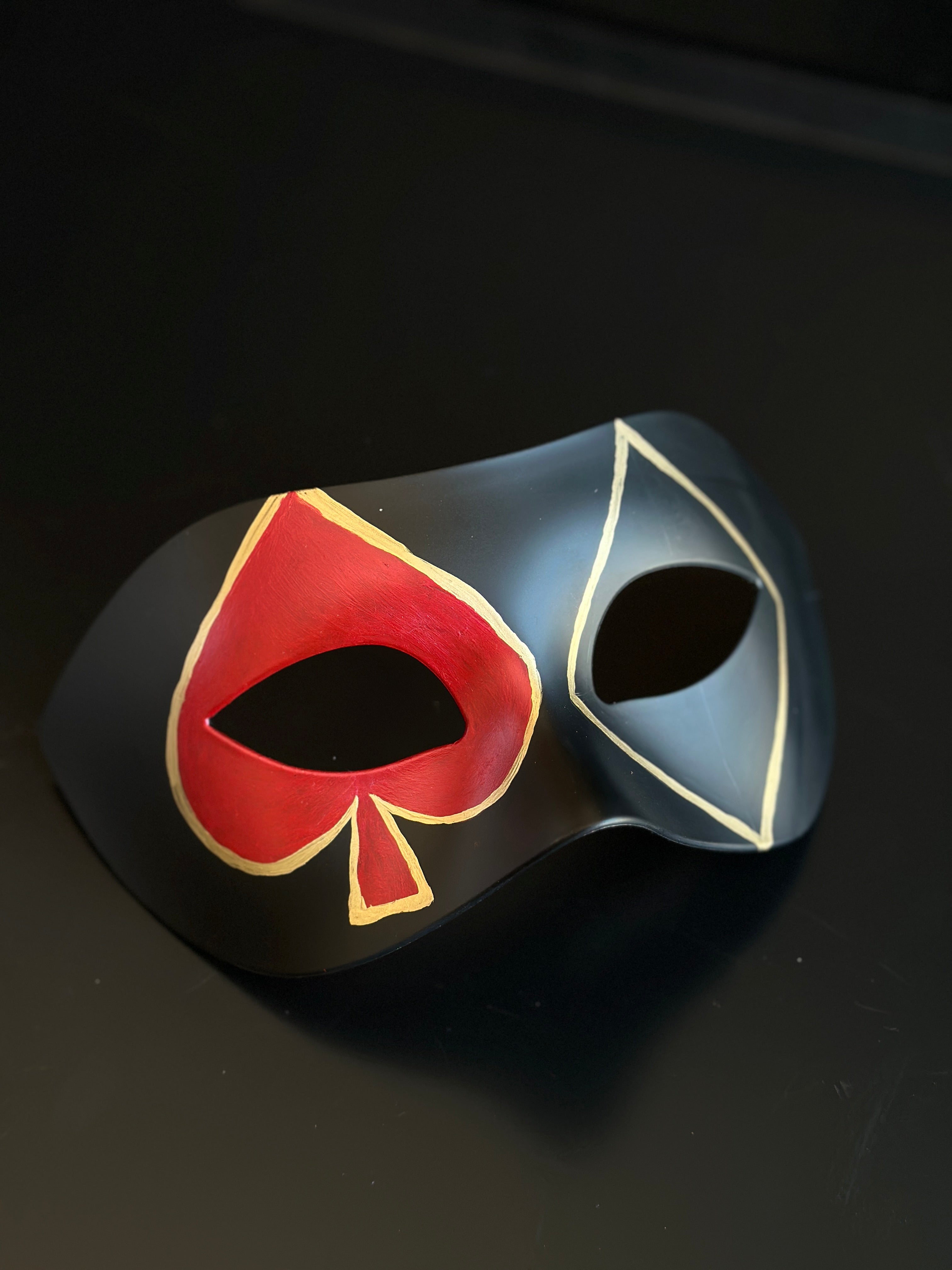 Black casino masquerade mask with red spade motif and white-outlined diamond playing card design on Venetian eye-mask silhouette