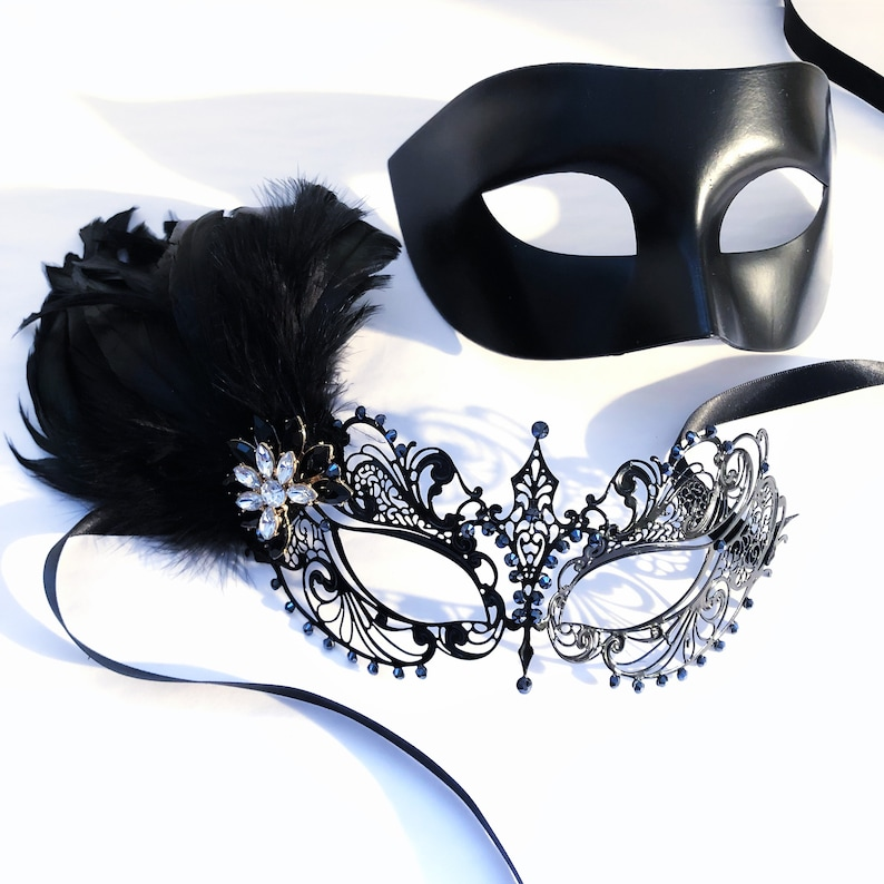 Black couples masquerade mask set with matte black men’s mask and filigree women’s mask with feathers, rhinestones, and jewel accent.