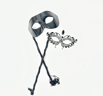 Black phantom-style men’s masquerade mask on stick with matching women’s rhinestone filigree mask, designed for elegant couple’s wear.