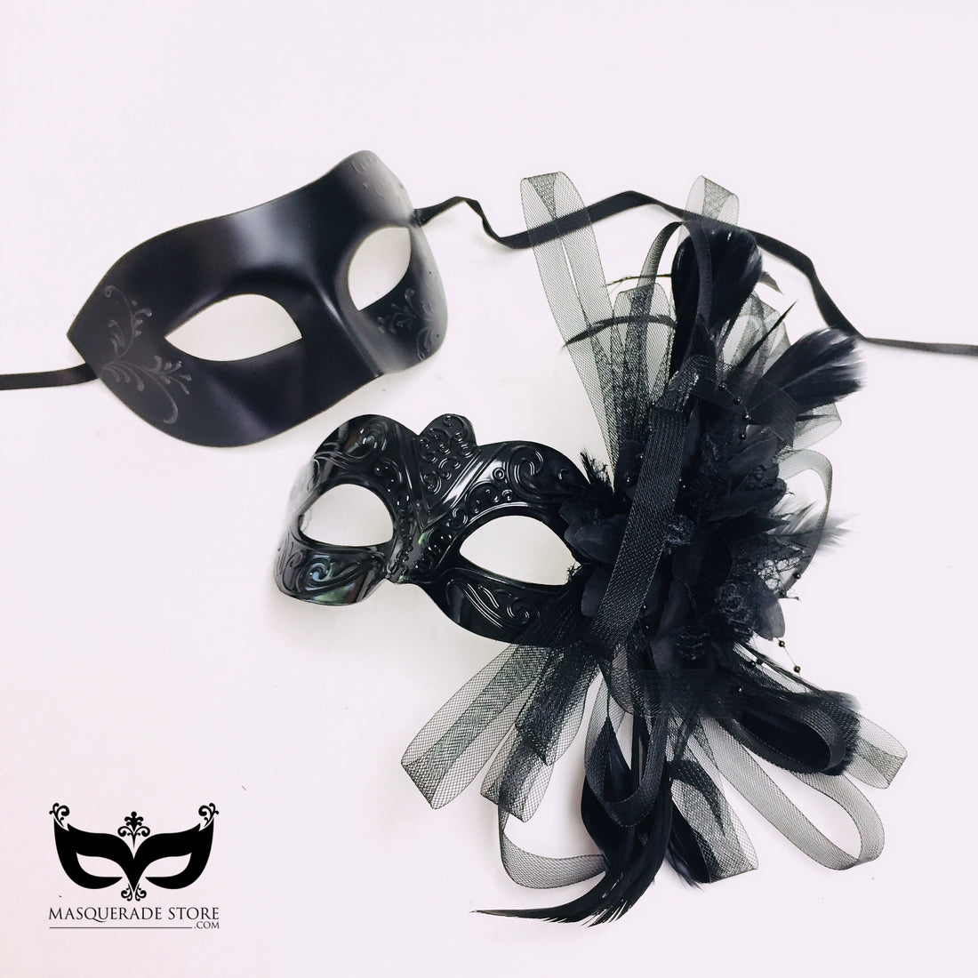 Black couples masquerade mask set with one sleek men’s mask and one women’s mask decorated with feathers and tulle.