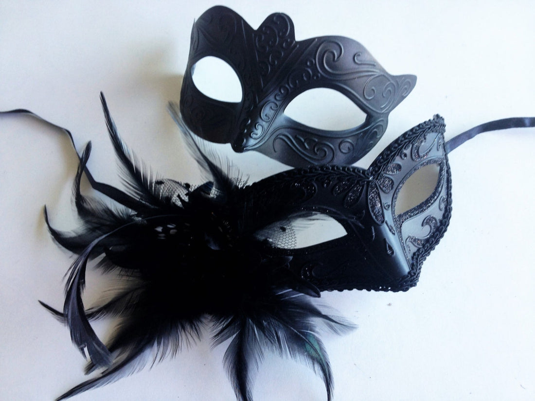 Black Venetian couples masquerade masks featuring a feather-accented mask for women and a cat-inspired scroll mask for men, ideal for masquerade balls and themed parties.

