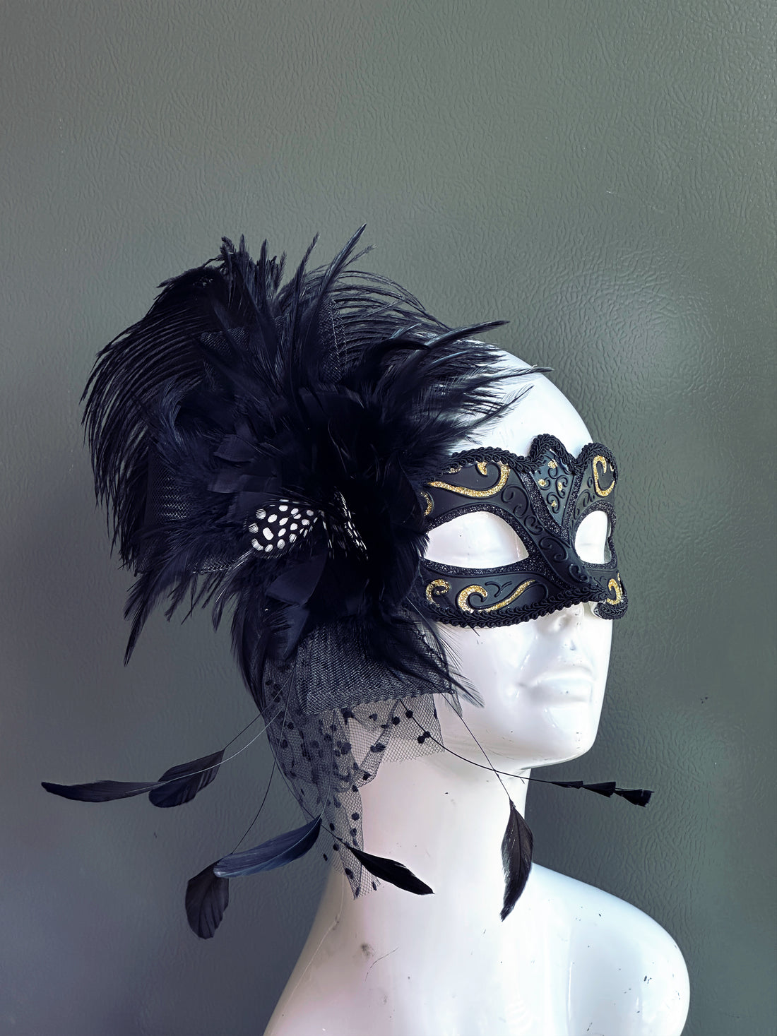 Elegant black feather masquerade mask with gold swirl accents and lace netting, perfect for Mardi Gras, Halloween, and masquerade balls.
