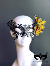 Black filigree masquerade mask with rhinestones and yellow butterfly accent, perfect for costumes and balls.
