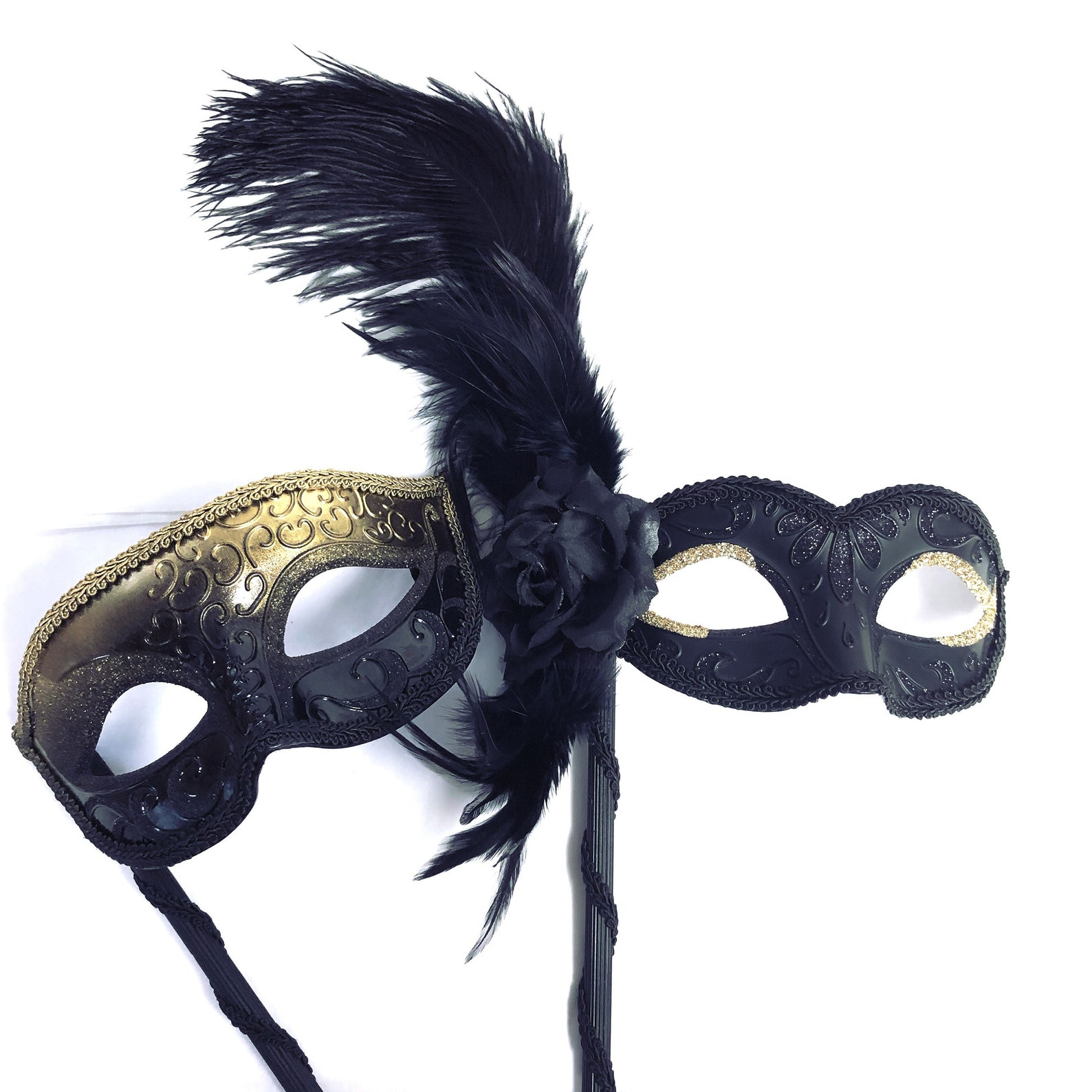 Black and gold masquerade couple’s mask set with a men’s gold scroll mask and a women’s handheld feather plume mask on a stick.