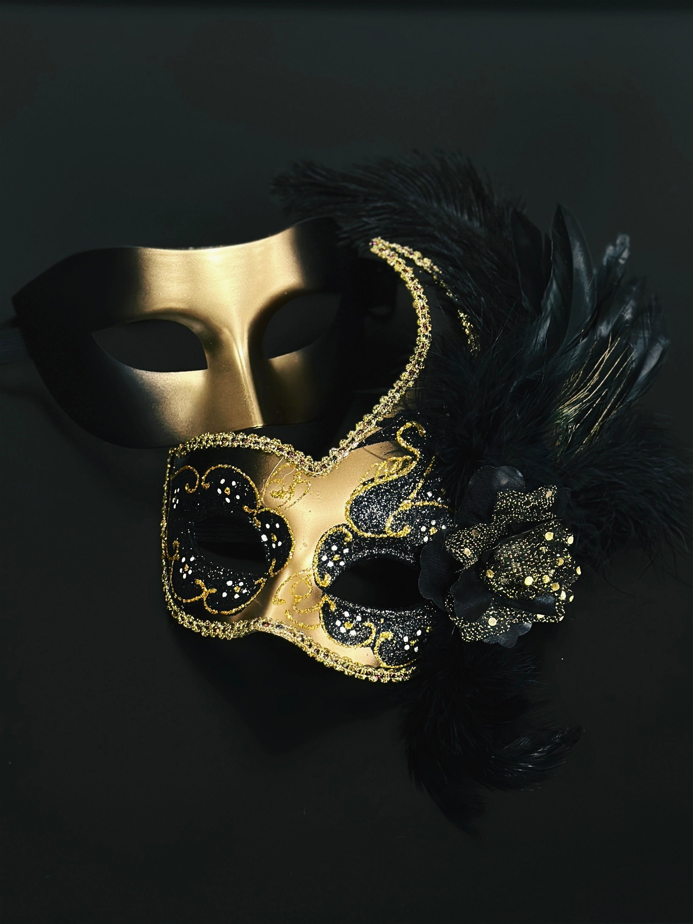 Black and gold masquerade couples masks, one with feathers and glitter floral detailing, perfect for Venetian balls, Mardi Gras, and prom.
