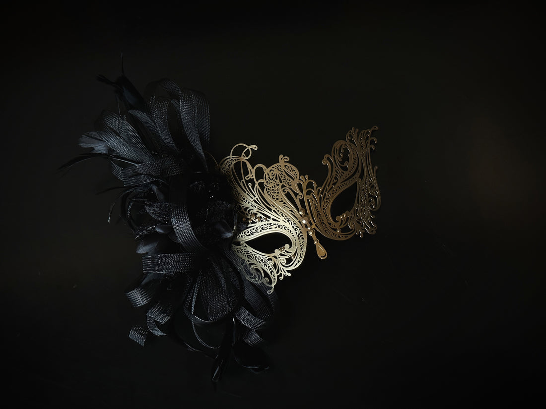Black and gold masquerade mask with filigree metal, tulle ribbon, and feathers, designed for proms and costume balls