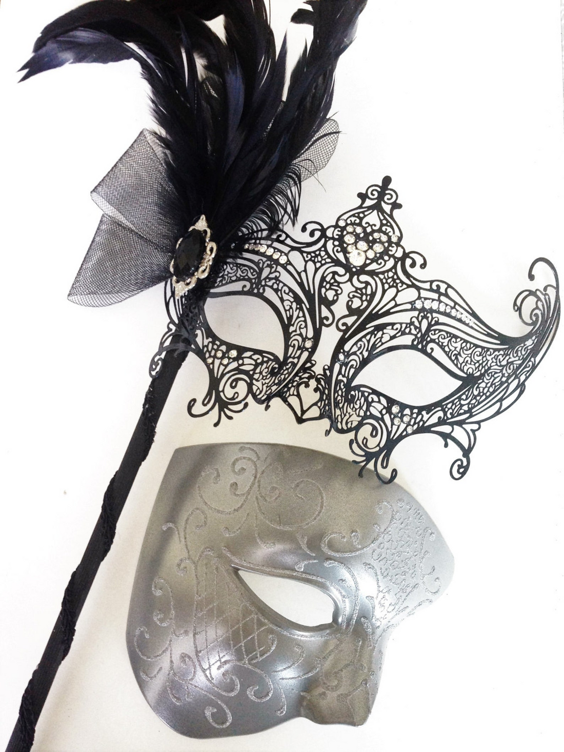 Couple’s masquerade mask set with a black lace handheld feather mask for women and a silver scrollwork mask for men.